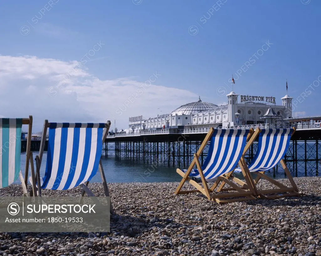 England, East Sussex, Brighton, Blue And White Striped Deckchairs On Pebble Beach Over Looking Brighton Pier.