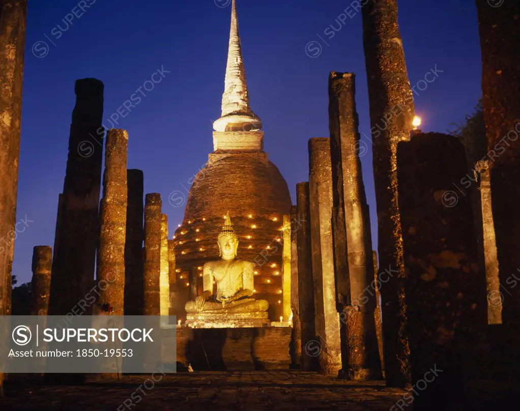 Thailand, Sukhothai, Colonnade Leading To Massive Seated Buddha And Stupa Illuminated At Dusk During Loi Krathong Festival Of Lights.