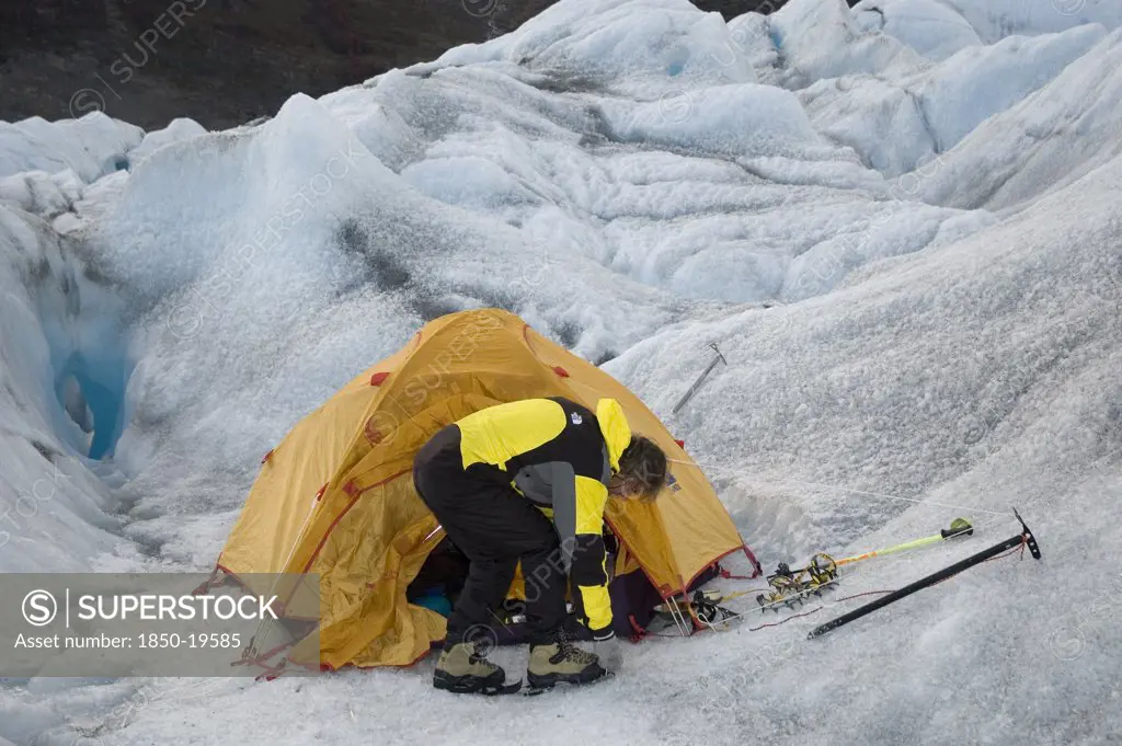 Chile, 'Southern Patagonia,', Glacier Chico, Mountaineer Attaching Crampons To His Boots In Front Of Tent Set Up In A Crevasse.Trek From Glacier Chico (Chile) To El Chalten (Argentina)