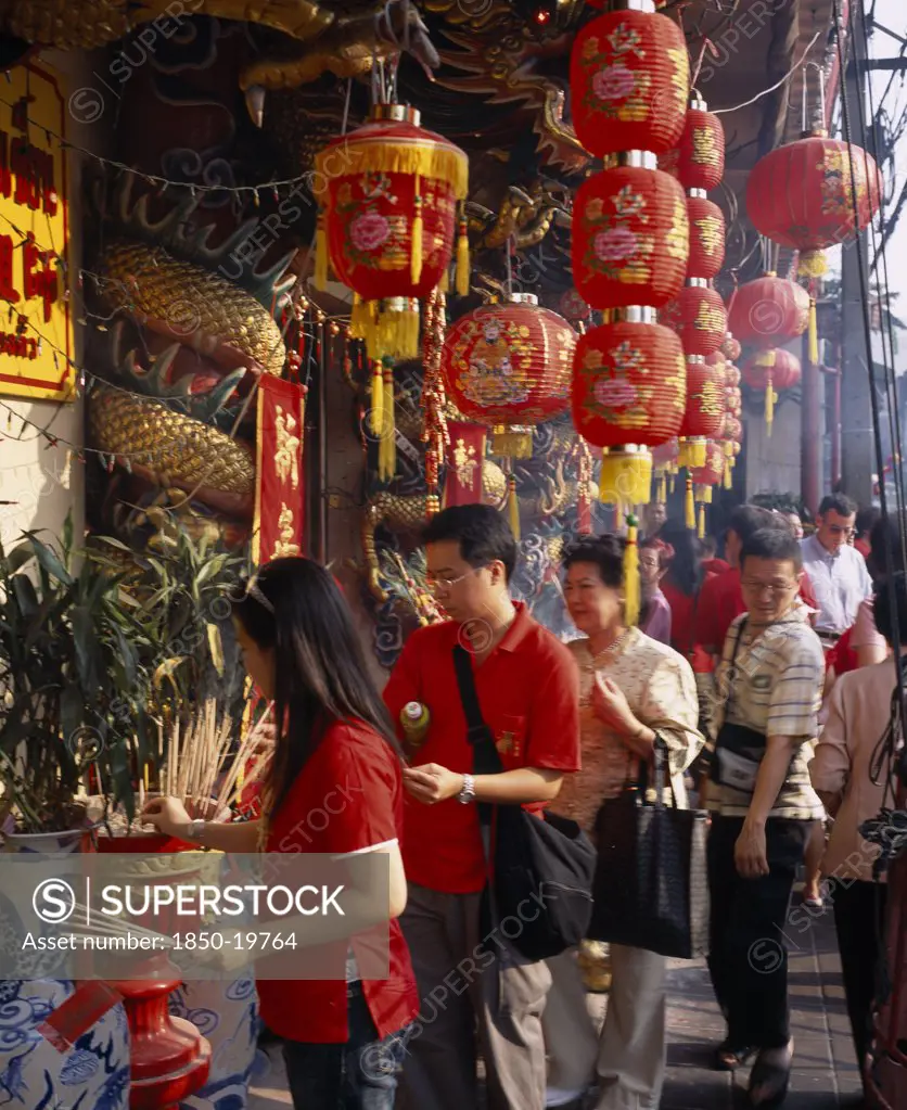 Thailand, Bangkok, China Town, Wat Traimit.  People Offering Prayers And Incense At Temple Decorated With Red Chinese Lanterns And Strings Of Coloured Lights For Chinese New Year.