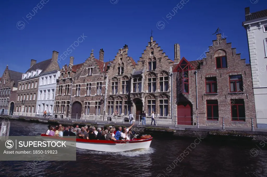Belgium, West Flanders, Bruges, Tourist Boat On Canal With Guide Pointing Out Traditional Waterside Architecture.