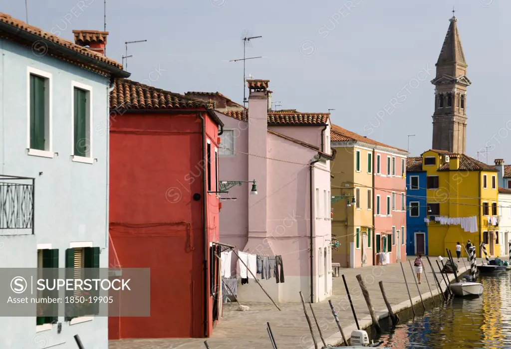 Italy, Veneto, Venice, Colourful Houses Beside A Canal On Burano. One Of The Few Inhabited Islands In The Lagoon. The Leaning Tower Of San Martino Church In The Distance