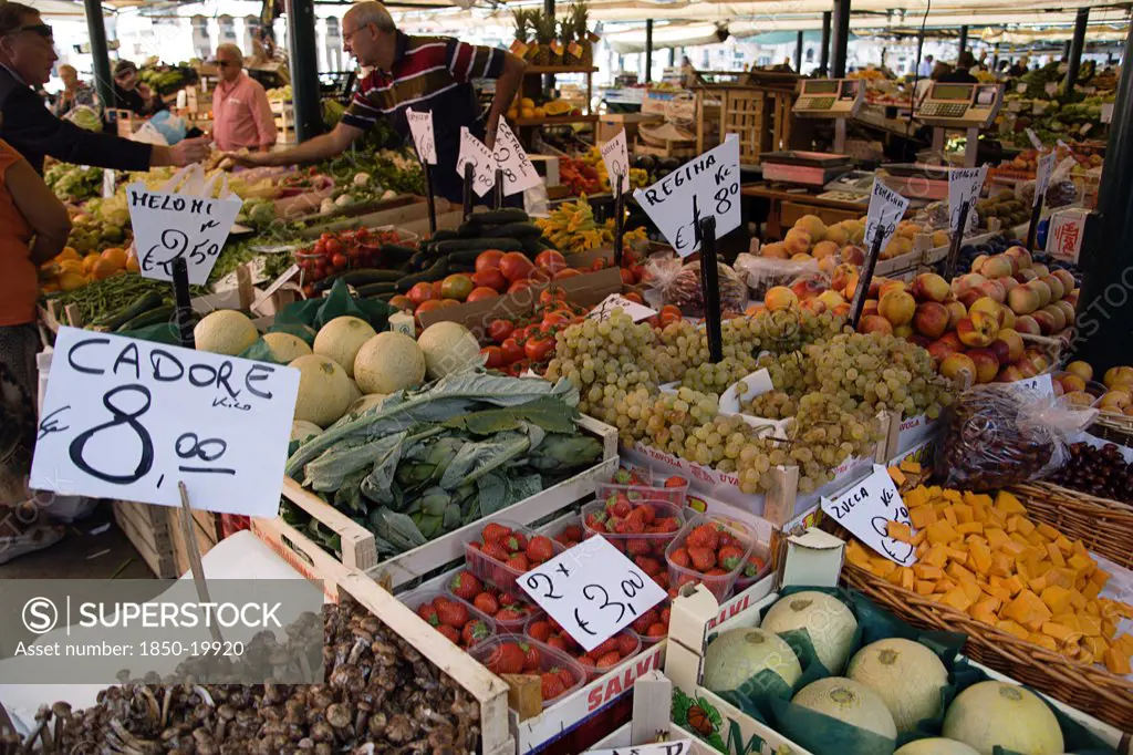 Italy, Veneto, Venice, The Vegetable Market With Vendor And Shoppers Beside The Produce In The San Polo And Santa Croce District Beside The Rialto Bridge On The Grand Canal