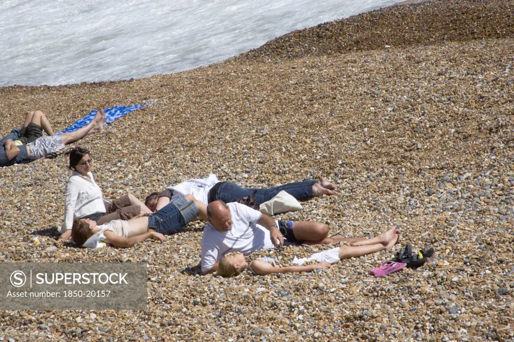 England, East Sussex, Brighton, Family On The Stoney Beach At Hove With Father Covering Son With Pebbles.