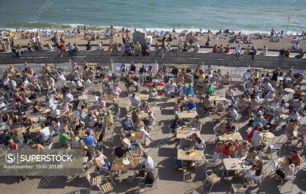 England, East Sussex, Brighton, People Sat At Tables Drinking Outside The Beach Seafront Bar.