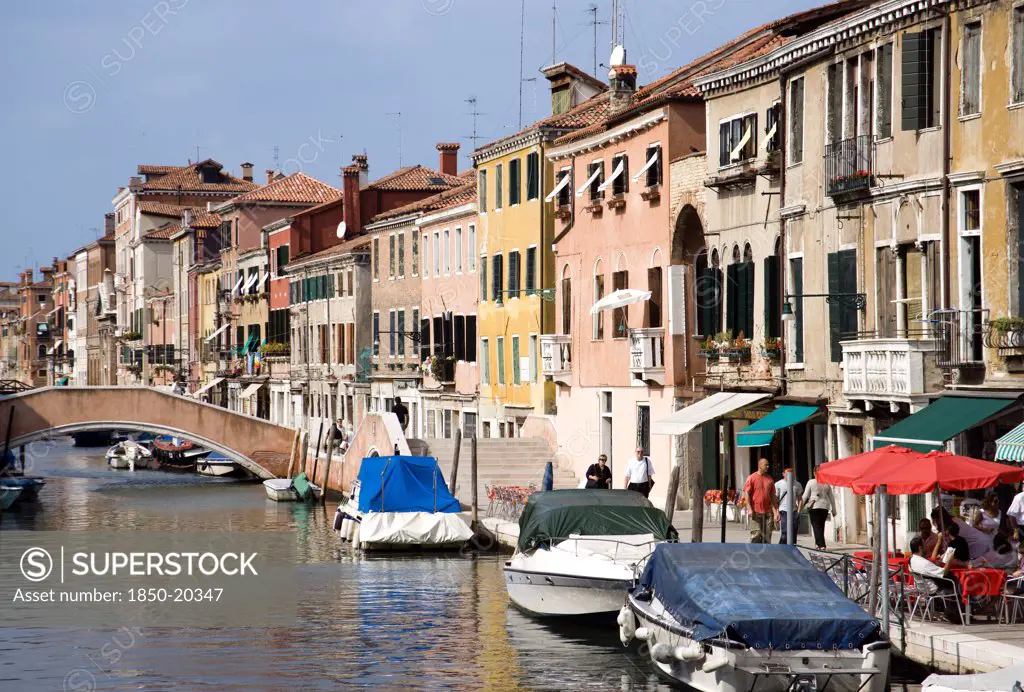 Italy, Veneto, Venice, Fondamenta Degli Ormesini In Cannaregio District With Boats Moored Along The Canal And People Walking Along The Pavement
