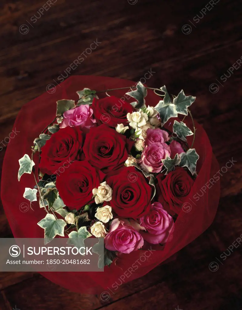Rose, Rosa 'Passion',Overhead view of a bouquet of six red roses with six pink and white roses with variegated ivy, surrounded by a red net wrap. 