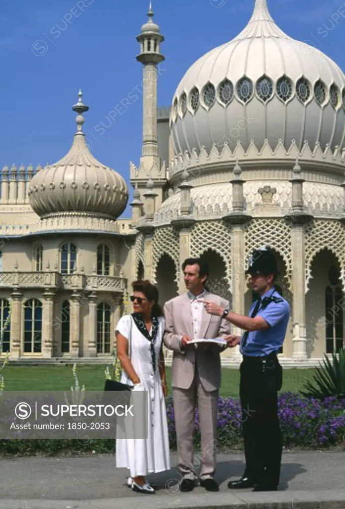 England, East Sussex, Brighton, Policeman Giving Tourist Couple Directions Outside The Royal Pavilion.