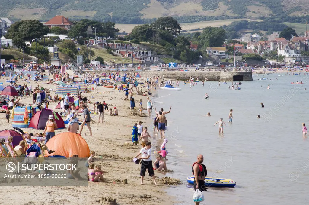 England, Dorset, Swanage Bay, View Along The Shoreline Of Sandy Beach With Sunbathers On The Sand And Swimming In The Sea