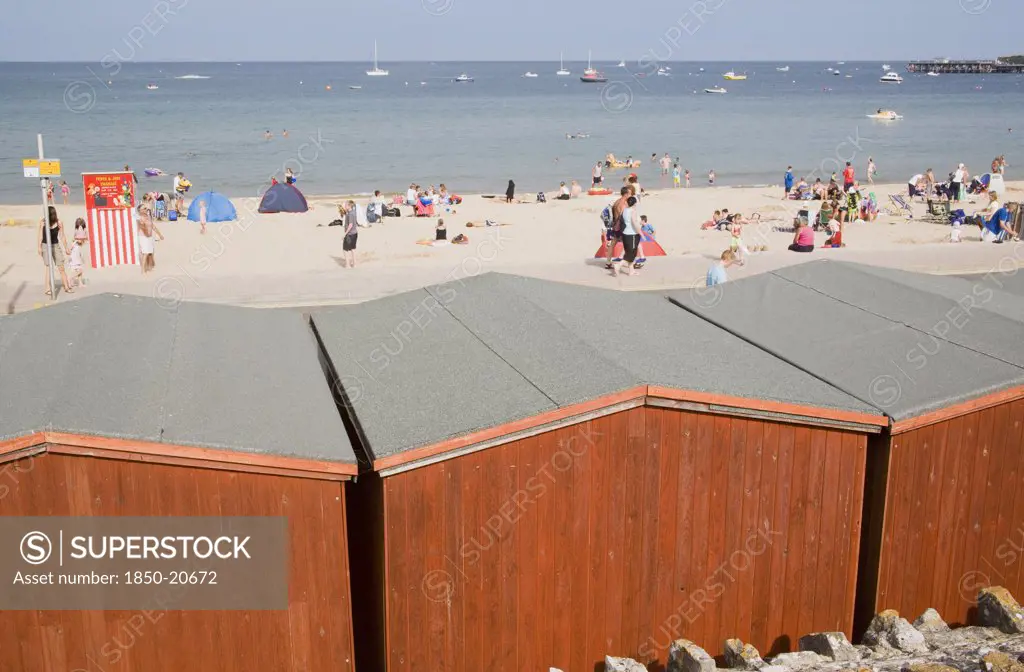 England, Dorset, Swanage Bay, View Across Beach Hut Roofs Towards Busy Sandy Beach And Sea
