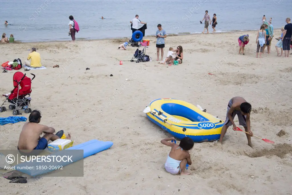 England, Dorset, Swanage Bay, Sunbathers And Children Playing On Sandy Beach Near Inflatables And A Dingy Boat