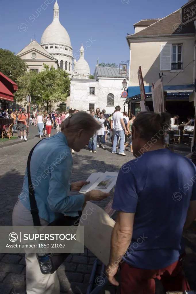France, Ile De France, Paris, Montmartre Place Du Tertre A Square Beside The Church Of Sacre Couer With A Tourist Discussing A Painting With An Artist Vendor