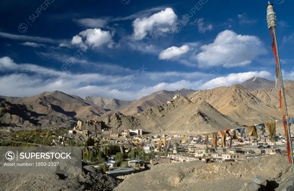 India, Ladakh, Leh Valley , Prayer Flags Hanging Above Village Set In Mountainous Landscape With Hilltop Palace In The Distance