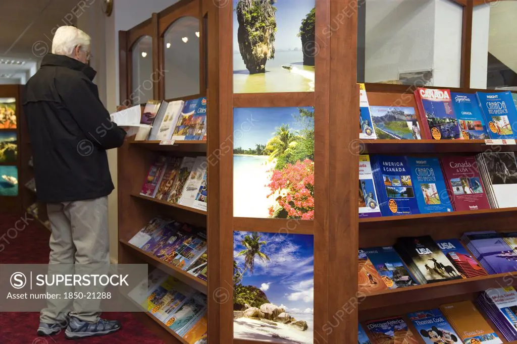 England, West Sussex, Chichester, Male Customer In A Travel Agents Office Looking Through Travel Brochures Displayed On Shelves