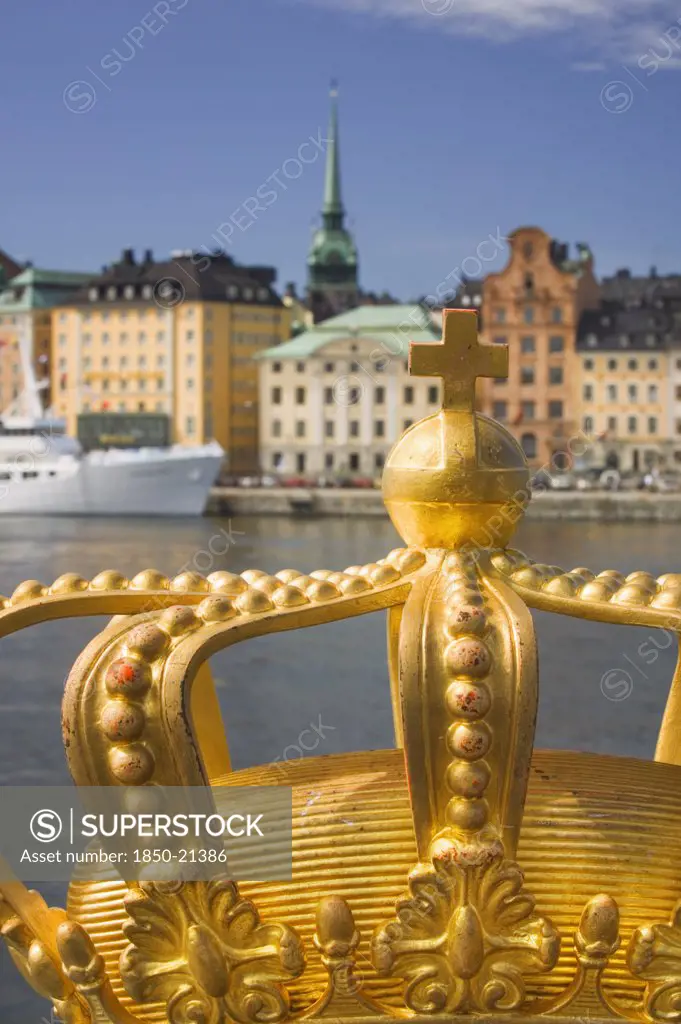 Sweden, Stockholm, Close-Up Of An Ornamental Crown On Skeppsholmsbron With Gamla Stan In The Background.