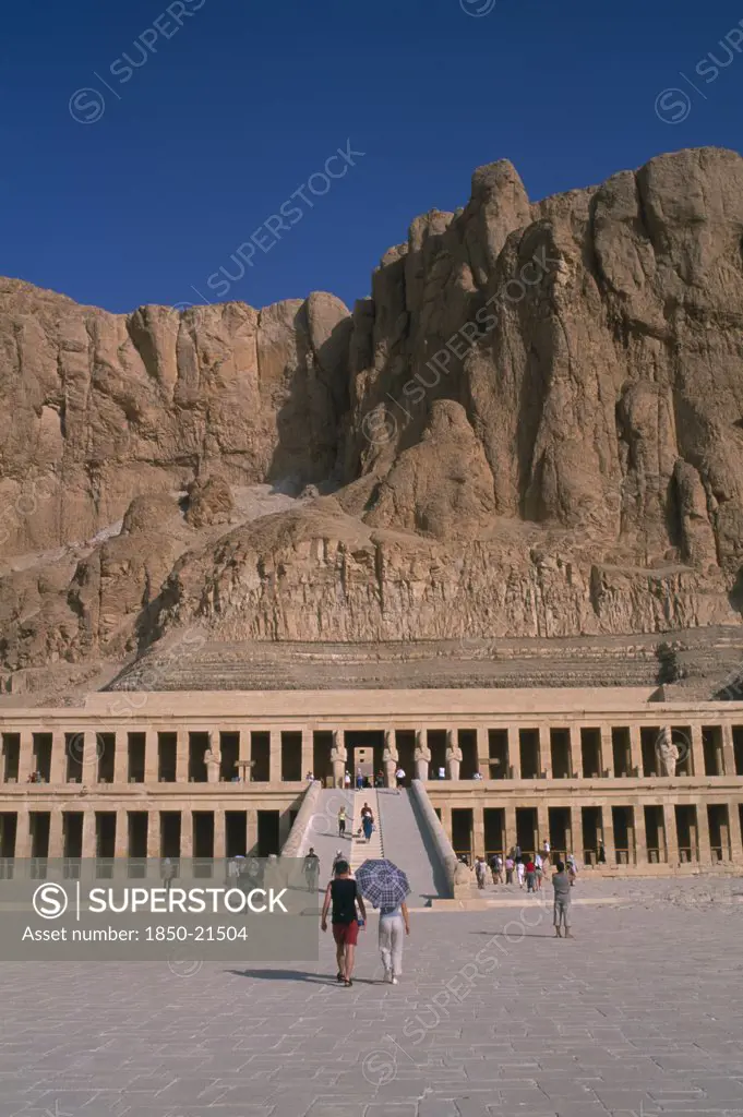 Egypt, Nile Valley, Thebes, Deir El-Bahri. Hatshepsut Mortuary Temple. Visitors Walking Towards Ramped Entrance With Limestone Cliffs Behind