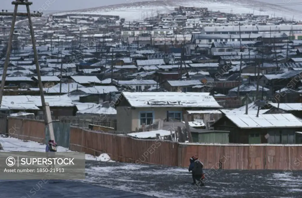 Mongolia, Ulan Bator, Snow Covered Rooftops Of Housing In City Suburbs In Winter With Children Wrapped Up In Warm Clothing Walking Along Road In Foreground.