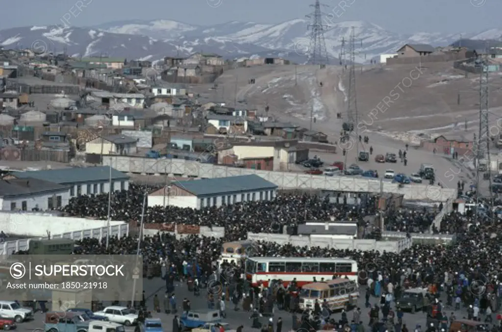 Mongolia, Ulan Bator, View Over Crowded Sunday Market With Houses Stretched Across Hillside Above And Line Of Pylons.