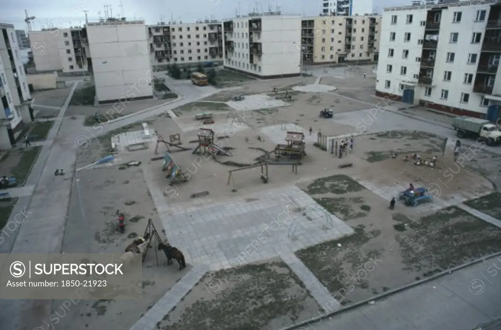Mongolia, Baga Noor, Multi Storey Housing In Coal Mining Town Surrounding Playground With Children Playing And Horses Tied To Street Light And Swing Frame.