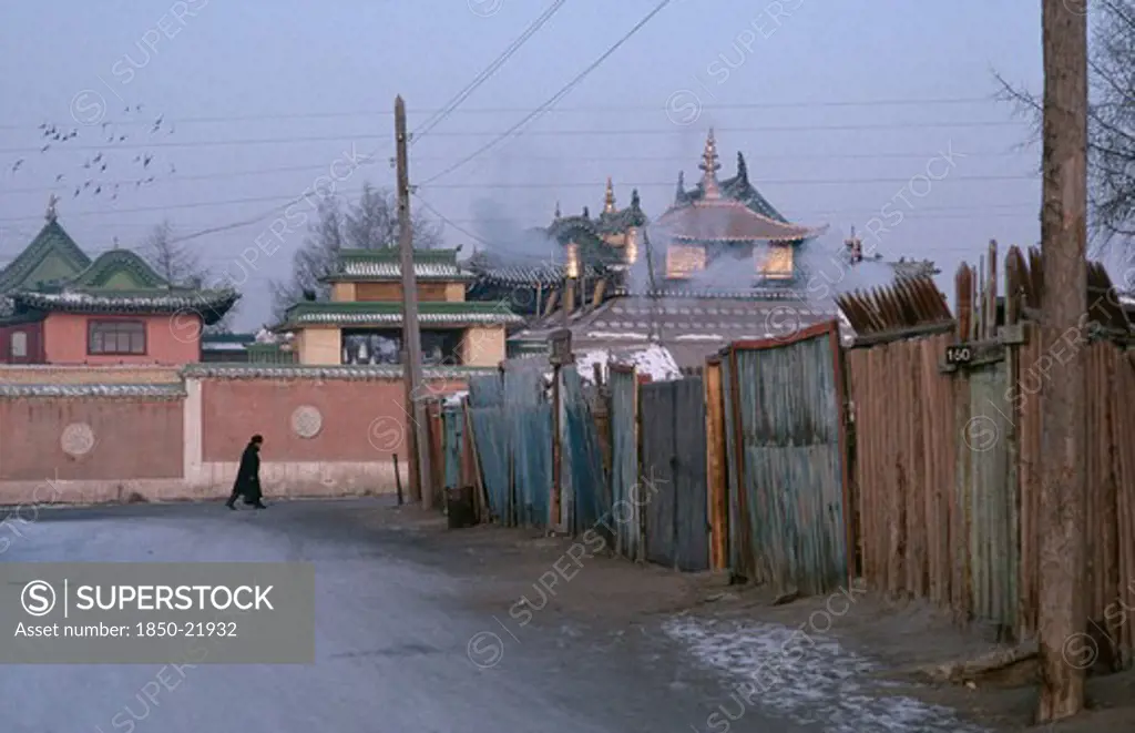 Mongolia, Ulan Bator, Gandan Monastery.  View Along Street Towards Monastery Rooftops With Passing Figure Wearing Winter Coat And Hat.