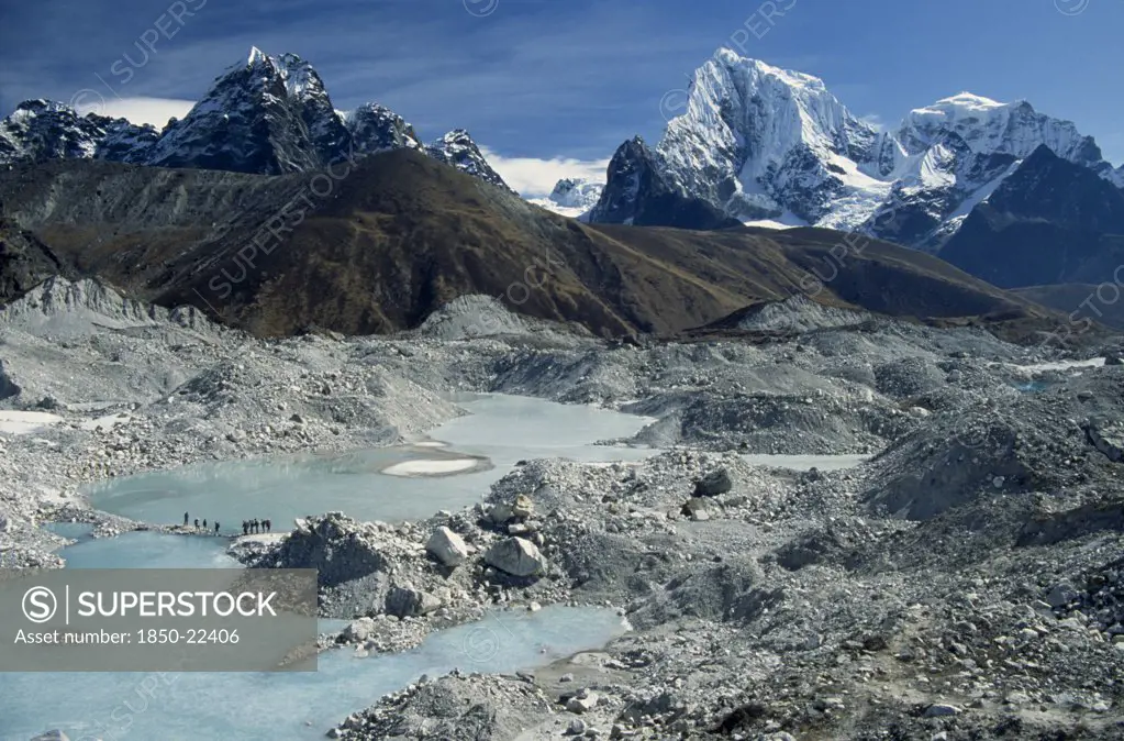 Nepal, Everest Trek, Near Gokyo, Trekkers Crossing An Ice Lake On The Ngozumpa Glacier With Mountains Cholatse On The Left And Tawachee On The Right In The Background.