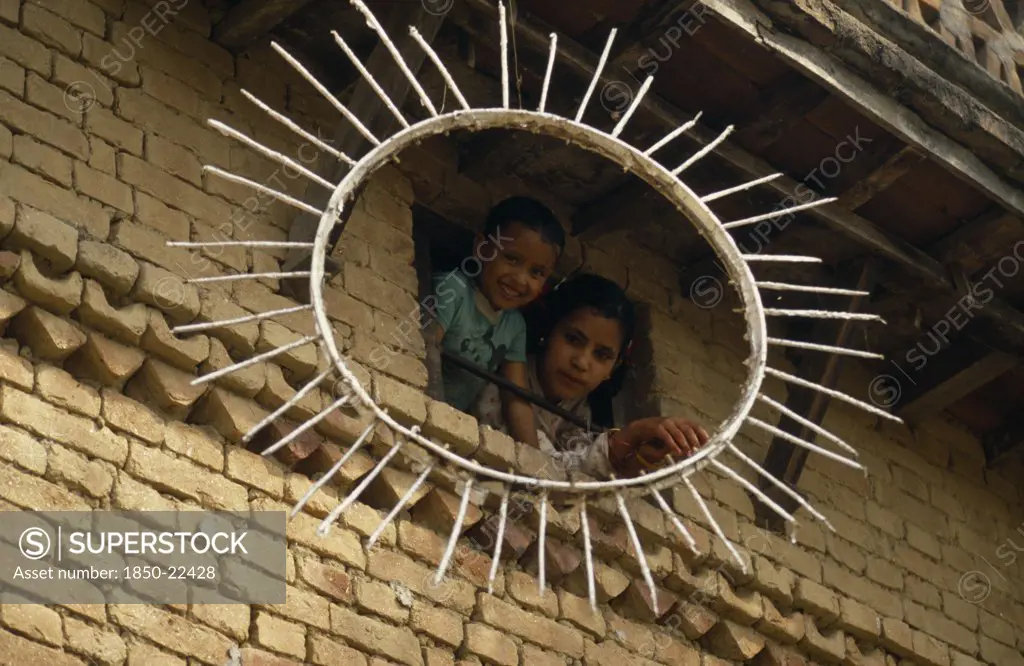Nepal, Kathmandu Valley, Children Looking Out Of A Window Framed By The Sun Symbol Of The Communist Party Of Nepal- United Marxist Leninists