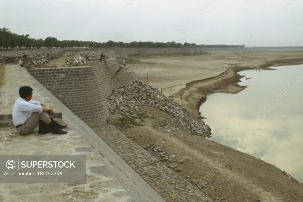 China, Jinan, Yellow River, Yellow River Dykes With Man Sat On Ground Looking Towards Water