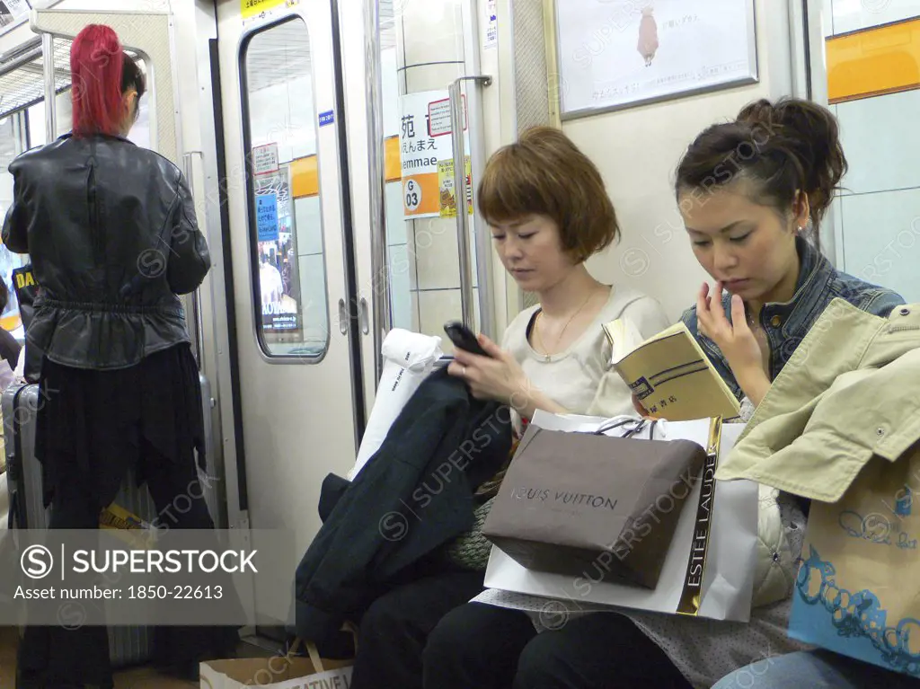 Japan, Honshu, Tokyo, 'Ginza - Three Women On A Subway Train, Right Side Young Woman, Shopping Bags Including Louis Vuitton, Woman In The Middle Using Cell Phone Text Message, Standing Woman (Left) With Bright Red Pony Tail, Dressed In Black'