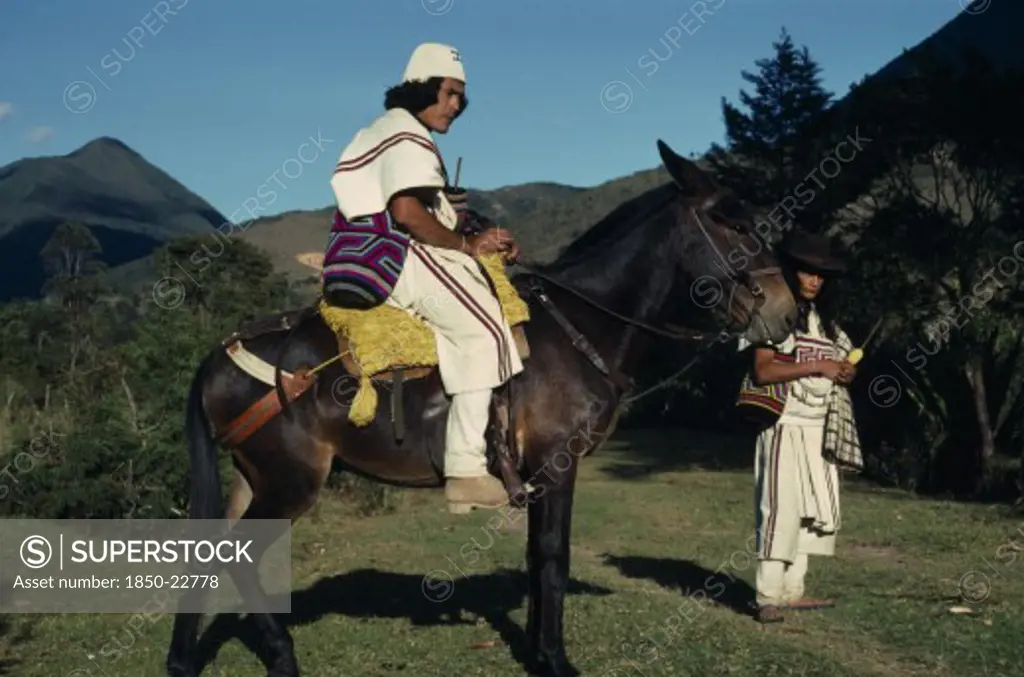 Colombia, Sierra Nevada De Santa Marta, Ika, Ika Leader Vicente Villafana On Mule With Another Man Standing At His Side  Both In Traditional Dress Of Woven Wool&Cotton Mantas Cloaks  Mochilas Shoulder Carrying Bags. Vicente Wears A Woven Cactus Fibre Helmet.  Arhuaco Aruaco Indigenous Tribe American Colombian Colombia Hispanic Indegent Latin America Latino Male Men Guy Scenic South America  Arhuaco Aruaco Indigenous Tribe American Colombian Columbia Hispanic Indegent Latin America Latino Male Me