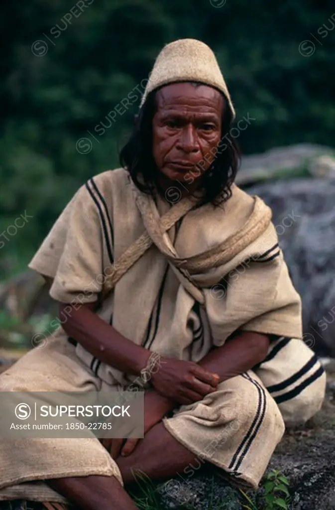 Colombia, Sierra Nevada De Santa Marta, Ika, Portrait Of Ika Mama Priest Juan De Jose Wearing Traditional Cactus Woven Cactus Fibre Helmet And Woven Wool&Cotton Manta Cloak And Trousers.Fine Spun Cotton Amulets On Wrist To Protect And Ward Off Evil. Arhuaco Aruaco Indigenous Tribe American Colombian Colombia Hispanic Indegent Latin America Latino Religion South America  Arhuaco Aruaco Indigenous Tribe American Colombian Columbia Hispanic Indegent Latin America Latino Religion South America One I