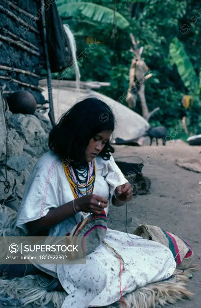 Colombia, Sierra Nevada De Santa Marta, Ika, Ika Girl Outside Her Home In The Sierra Sewing Traditional Woollen Mochila Shoulder Bag. Wears Traditional Woven Wool&Cotton Manta Cloak And A Necklace Of Many Strings Of Glass Beads - A Sign Of Wealth Arhuaco Aruaco Indigenous Tribe American Classic Classical Colombian Colombia Hispanic Historical Indegent Kids Latin America Latino Older South America  Arhuaco Aruaco Indigenous Tribe American Classic Classical Colombian Columbia Hispanic Historical I