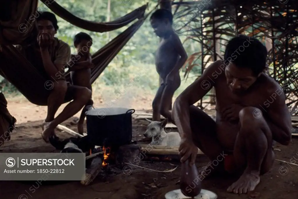 Colombia, North West Amazon, Vaupes, Maku Indian Men And Children Inside Palm-Thatched Shelter/Home With Hunting Dogs Lying Beside Open Fire And Cooking Pot. Indigenous Tribe Indian Nomadic American Colombian Columbia Hispanic Indegent Kids Latin America Latino Male Man Guy South America Vaupes Male Men Guy Vaupes