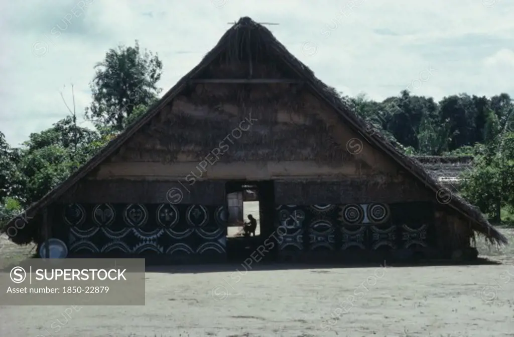 Colombia, North West Amazon, Tukano Indigenous People, Makuna Communal Home Or Maloca With White And Yellow Clay And  Charcoal Painted Design On Exterior Facade.  Man Basket-Making Silhouetted In Rear Women'S Entrance.Tukano  Makuna Indian North Western Amazonia Maloca American Colombian Columbia Hispanic Indegent Latin America Latino Male Men Guy South America Tukano