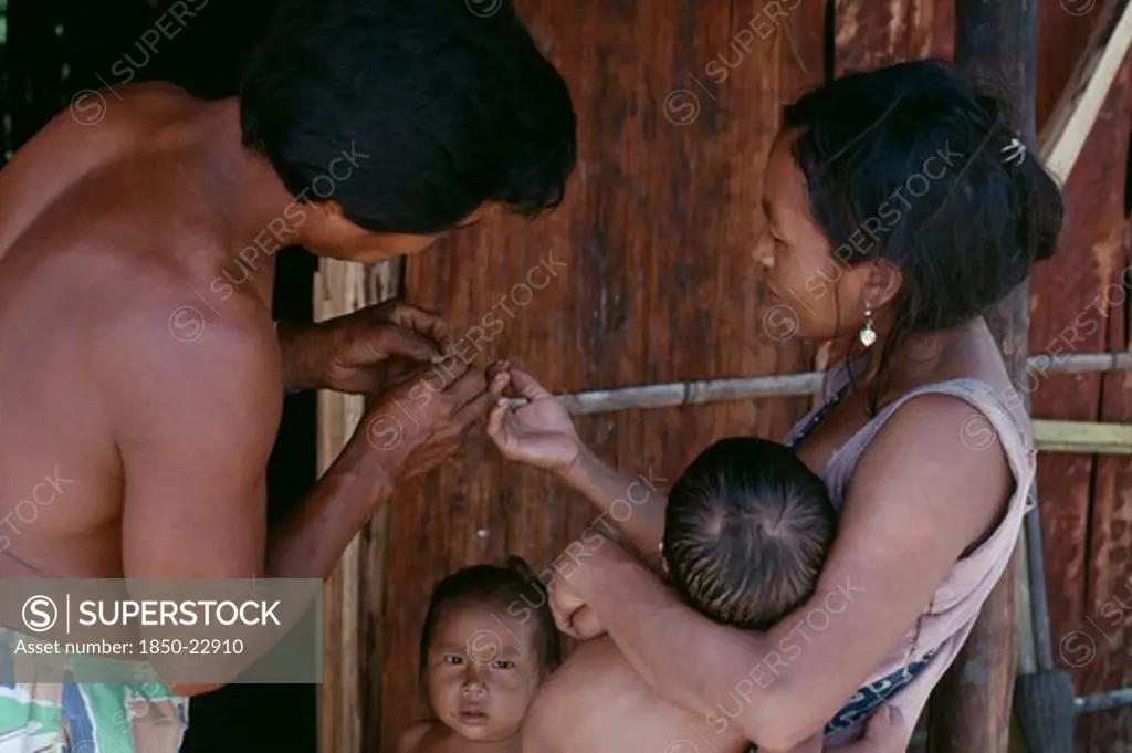 Colombia, North West Amazon, Tukano Indigenous People, Makuna Family.  Venancio Removing Thorn From His Wife'S Finger With Two Young Children Partly Seen. Tukano  Makuna Indian North Western Amazonia American Colombian Columbia Hispanic Indegent Kids Latin America Latino South America Tukano