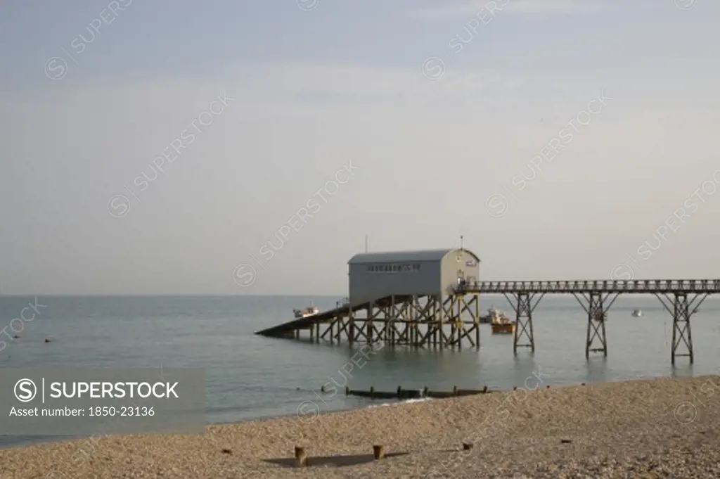 England, West Sussex, Selsey, Royal National Lifeboat Institution. View Across Shingle Beach Towards A Pier With Rnli Station