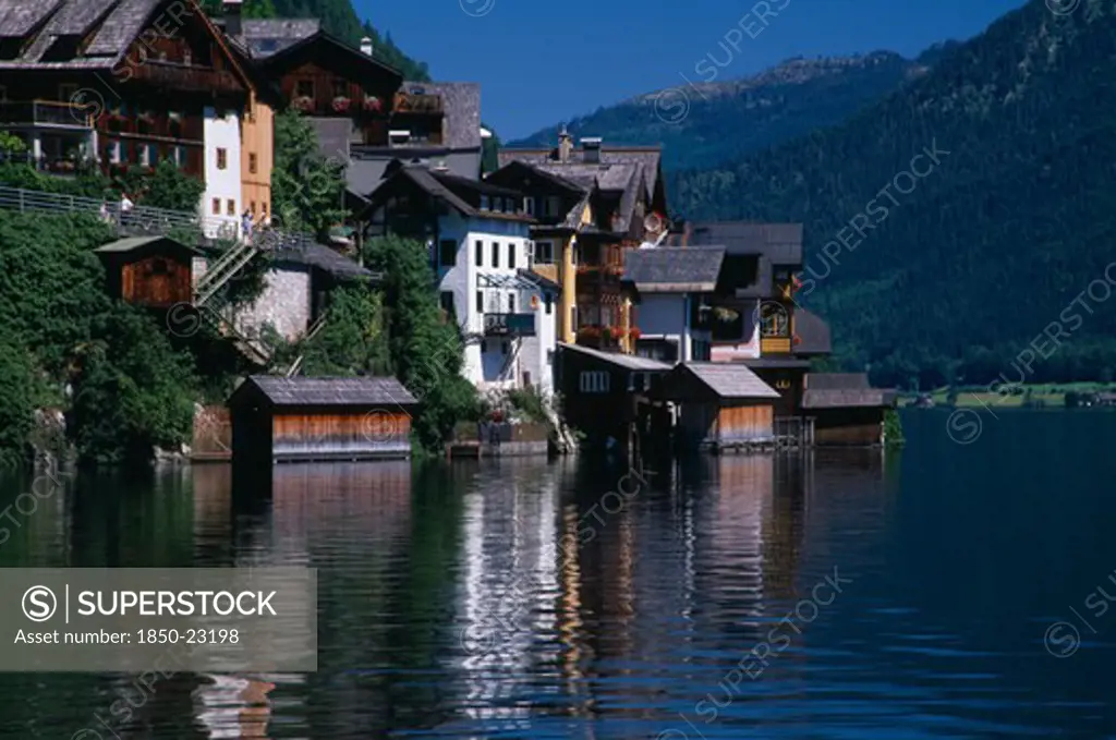 Austria, Oberosterreich, Hallstatt, Typical Architecture And Boat Houses On Shore Of Hallstattersee Lake And Reflected In Rippled Surface.