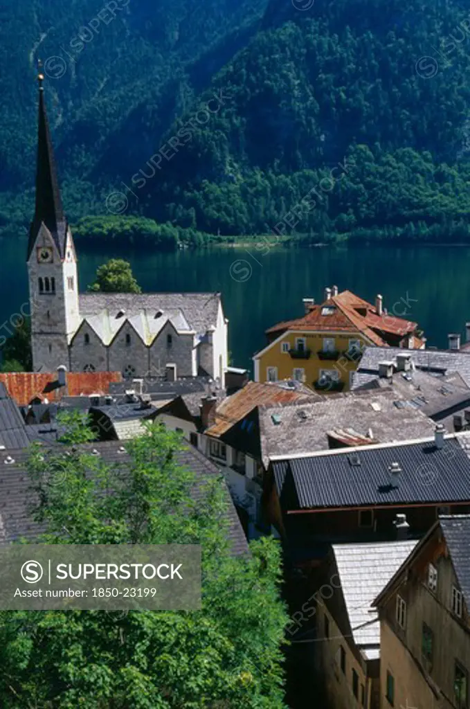Austria, Oberosterreich, Hallstatt, 'View Over Tiled Village Rooftops, Hotel And Church With Hallstattersee Lake And Steep Mountain Backdrop.'