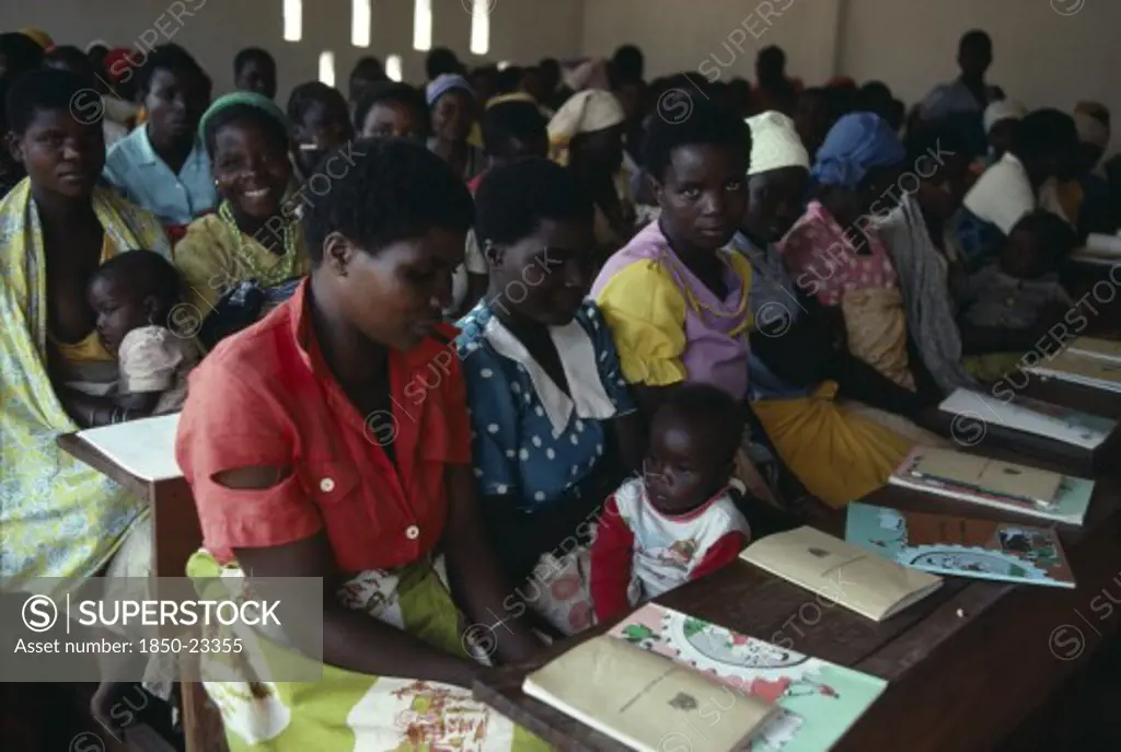 Malawi, Adult Education, 'Adult Literacy Class For Refugees From Mozambique In Kunyinda Camp.  Classroom Of Young Women, Some With Children Sitting At Long Wooden Desks.'