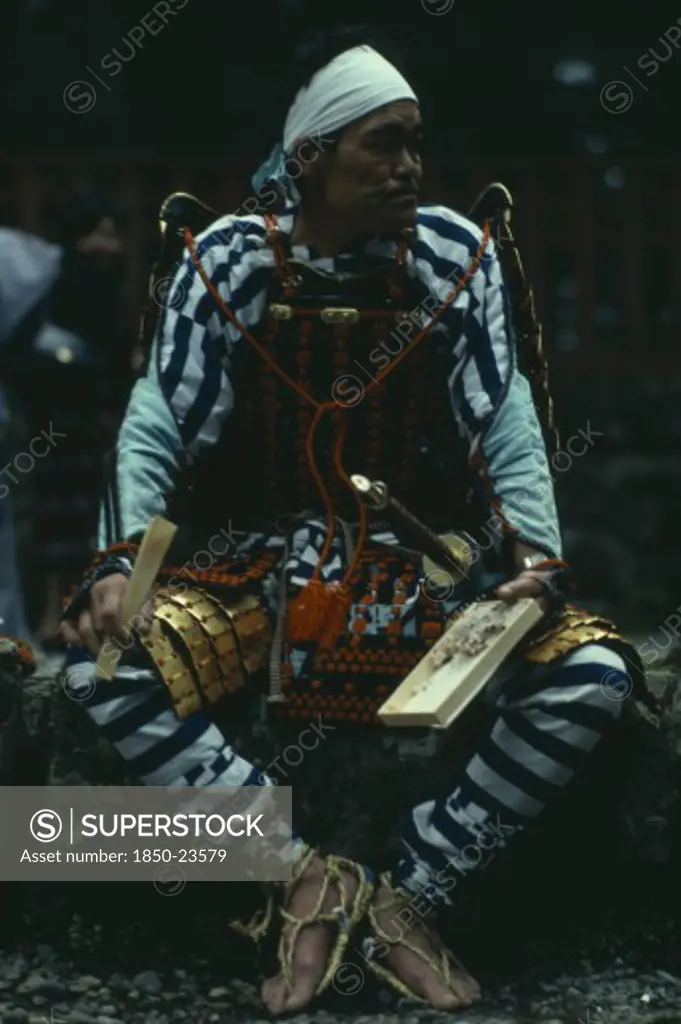 Japan, People, Samurai, 'Portrait Of Samurai Wearing Armour Constructed Of Plates Of Metal Or Bamboo Held Together With Coloured Lacing, Rope Sandals And White Cloth Head Band With Sword At Side.  Seated, Holding Bento Lunchbox And Chopsticks.  '