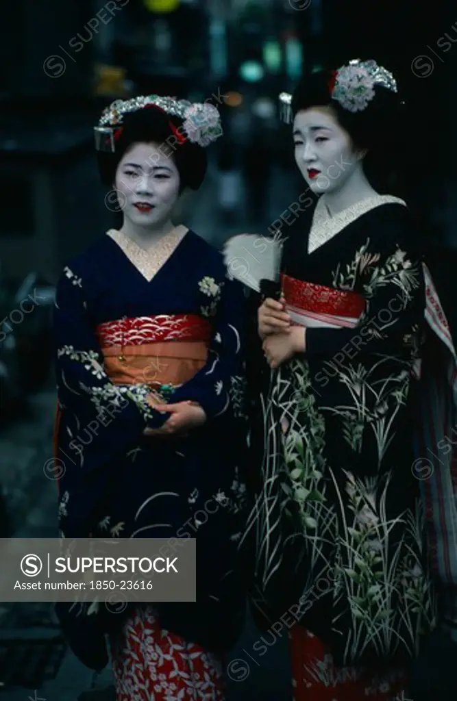 Japan, Customs, Geisha, Two Maiko Or Apprentice Geisha With White Powdered Faces And Red Painted Lips Wearing Richly Embroidered Kimonos And Decorative Hair Pieces.