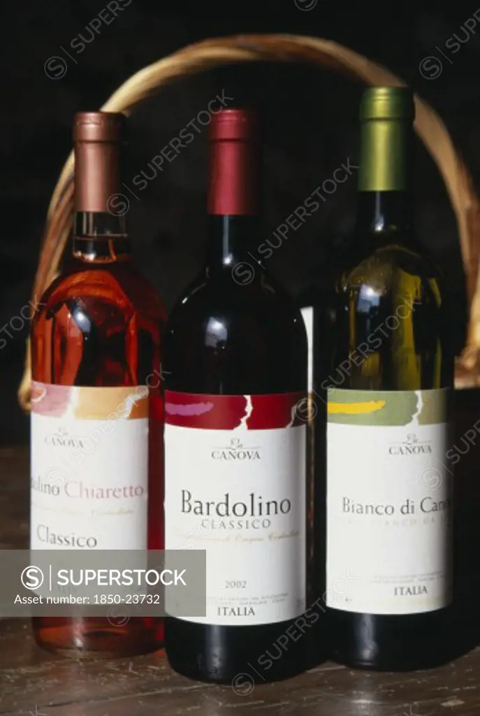 Italy, Veneto, Lake Garda, 'Bardolino.  Bottles Of Red, White And Rose Wine From The Bardolino Region Displayed In Front Of Basket And Framed By Handle.'