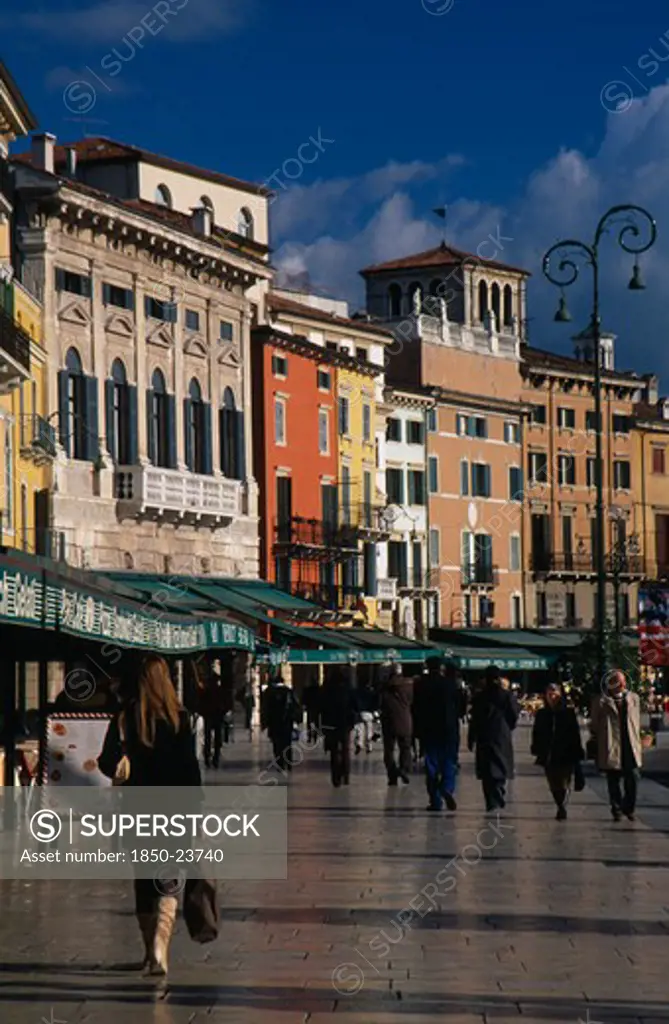 Italy, Veneto, Verona, Piazza Bra.  People Walking Past Line Of Bars And Cafes And Painted Facades Of Architecture Overlooking Square.