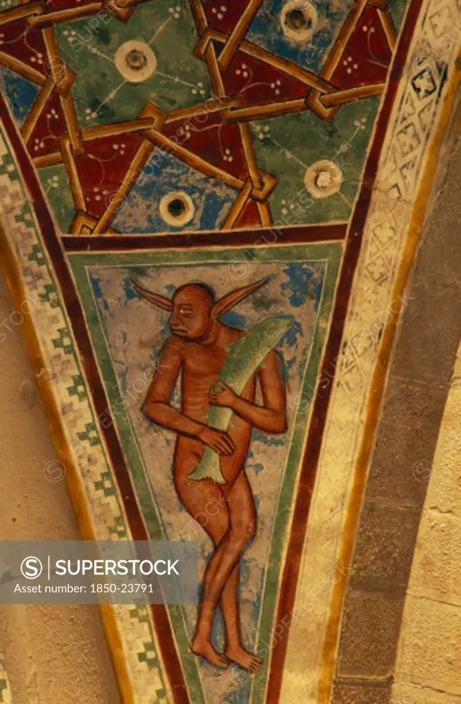 Italy, Lombardy, Lake Maggiore, Angera.  Architectural Detail And Painting In Rocca Di Angera Medieval Castle Depicting Figure Carrying Fish And Abstract Pattern Set In Space Between Arches Or Spandrel