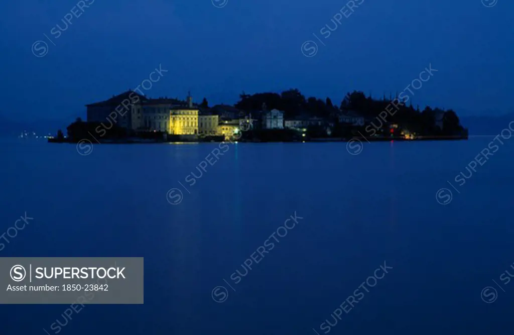 Italy, Piedmont, Lake Maggiore, Borromeo Islands.  View Across Lake Towards Small Rocky Island Of Isola Bella With Palazzo Borromeo Illuminated At Night.
