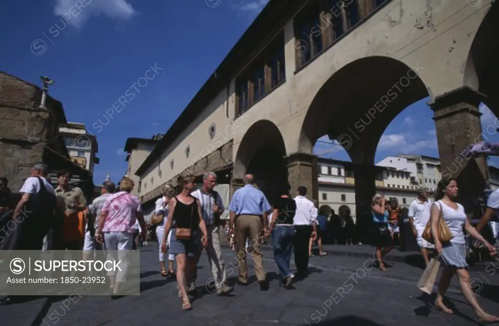 Italy, Tuscany, Florence, Ponte Vecchio Bridge With Visitors Walking Along Street Lined With Shops And Stalls By The Bridge Arches