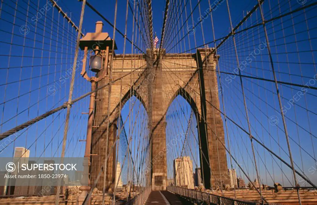 Usa, New York, New York City, Brooklyn Bridge.  View Across Bridge Towards Manhattan Skyline Part Framed By Central Stone Tower And Intersected By Steel Wires And Suspension Cables. Spans The East River.  Construction Began In 1870 And The Bridge Opened For Use In 1883.