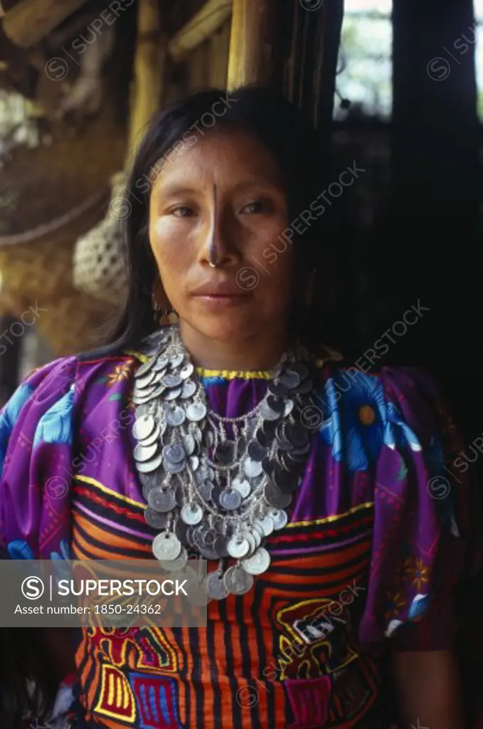 Colombia, Darien, Kuna Indigenous Tribe, Three-Quarter Portrait Of Kuna Indian Woman From The Arquia Community Wearing Traditional Mola Applique Layered Design Of Mythical Kuna Birds  Gold Nose Ring With Black Line Drawn Along Length Of Nose And A Silver Necklace Of Old Colombian And Panamanian Coins. Cuna