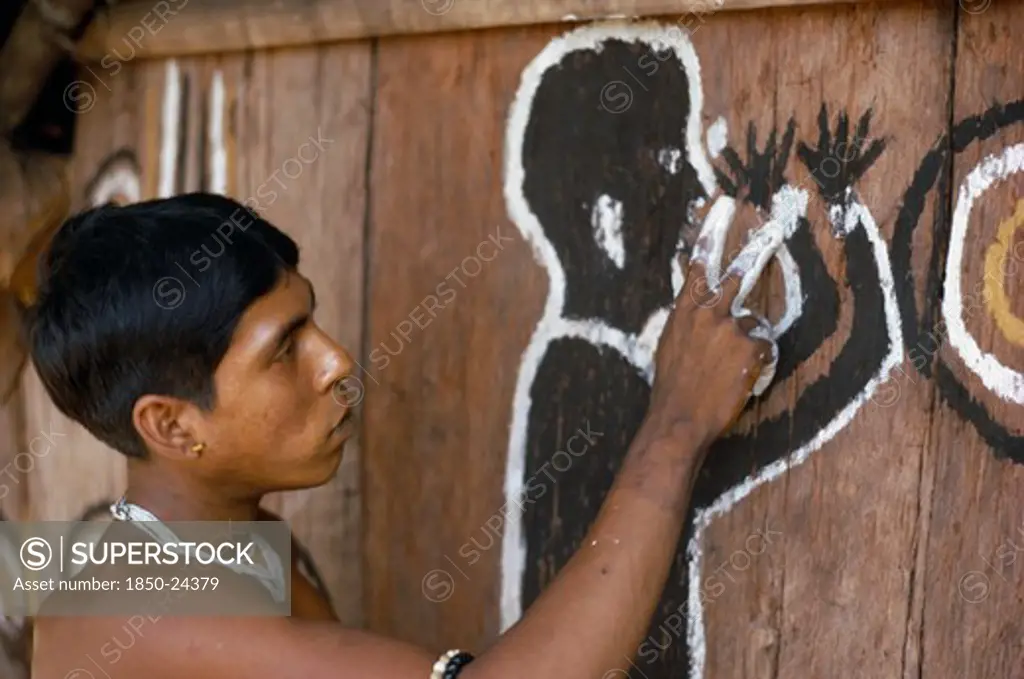 Colombia, North West Amazon, Tukano Indigenous Tribe, Barasana Man (Sub Group Of Tukano) Paints Front Of Maloca Large Communal Home. The Symbolic Shamanic Figure Is To Keep Evil Spirits And Bad Weather Away.