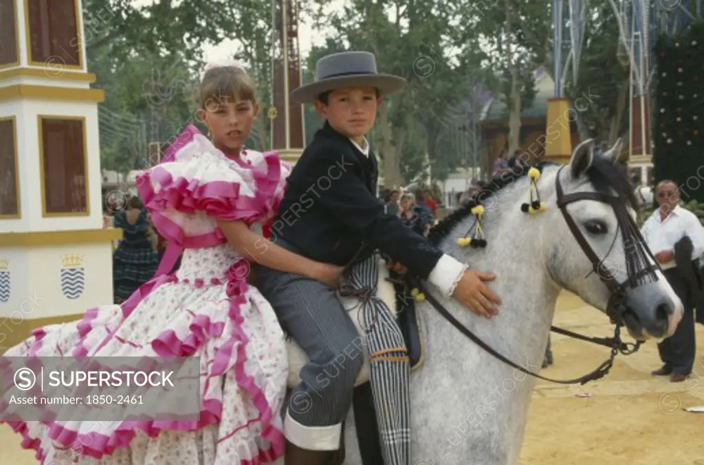 Spain, Andalucia, Jerz De La Frontera, Children In Flamenco Costume On A Grey Pony At Jerez Horse Fair.