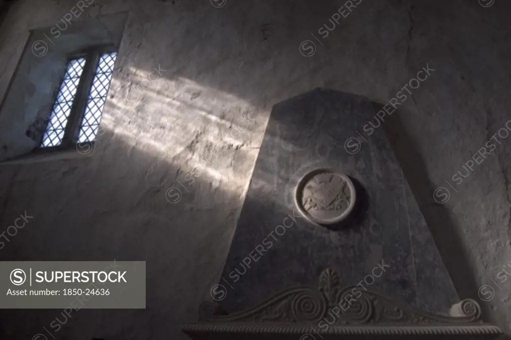 England, West Sussex, Boxgrove, Boxgrove Priory Church Of St Mary And St Blaise. Interior View Of  Light Shining Through Small Window Onto A Wall And Marble Monument.